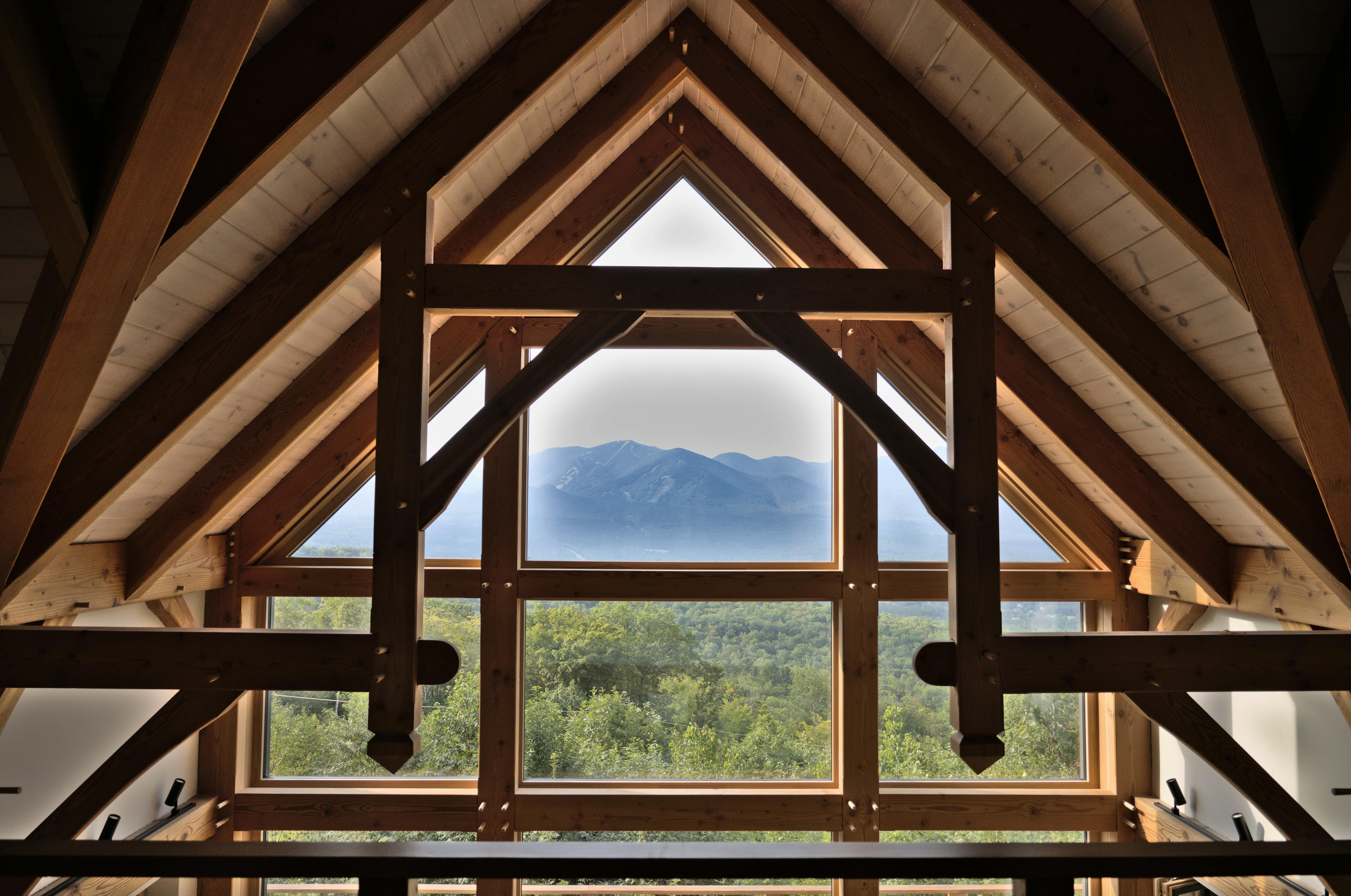 Rustic wooden interior showcasing timber trusses with a stunning mountain view through large windows.