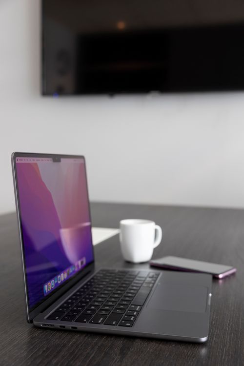 Free Stylish workspace featuring a laptop, smartphone, and coffee cup on a wooden table. Stock Photo