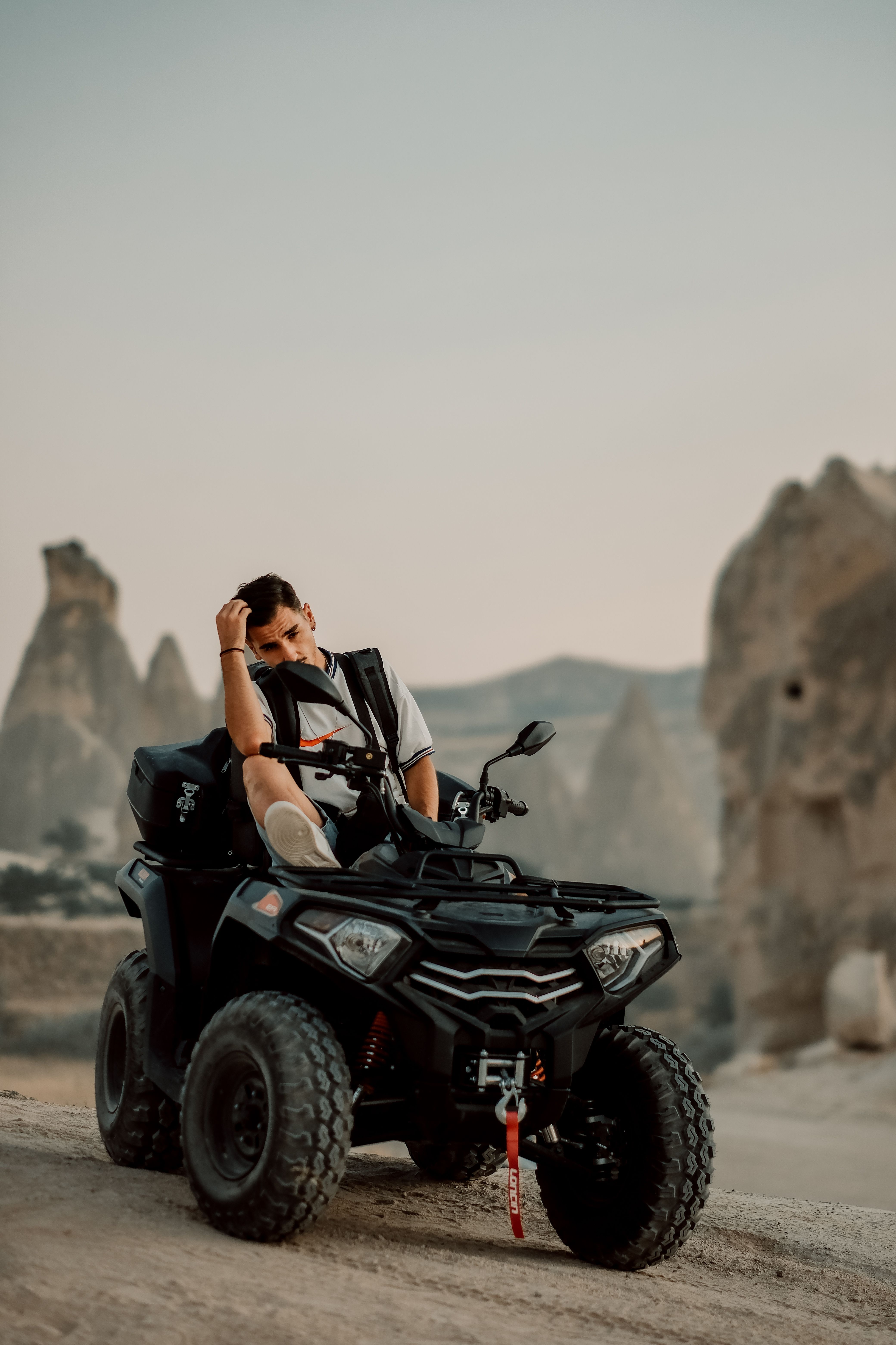 A man sitting on an ATV with stunning mountain formations in the background during daytime.