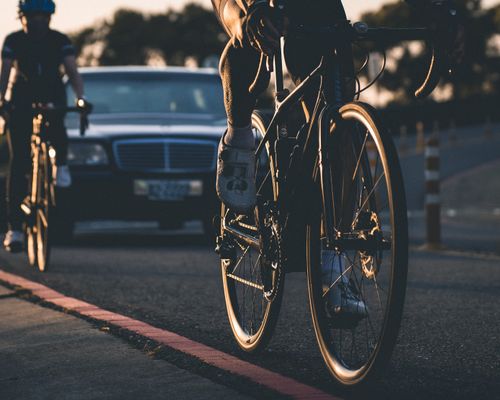 Free A dynamic close-up of a cyclist biking on the road at sunset with a car in the background. Stock Photo