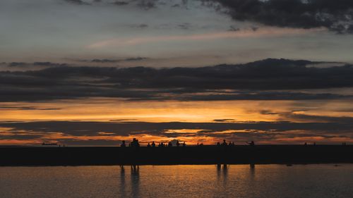 Free Calm beach scene at sunset with silhouetted figures and vibrant sky reflections. Stock Photo
