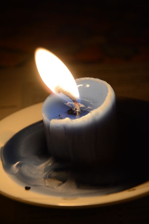 Free Close-up of a burning blue candle with melting wax creating a warm glow in the darkness. Stock Photo