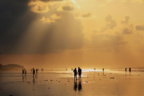 Free Silhouettes of people enjoying a peaceful sunset on Mandarmani Beach, India with a stunning golden sky. Stock Photo