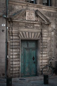 A weathered ornate stone doorway with a parked bicycle, depicting classic European architecture.