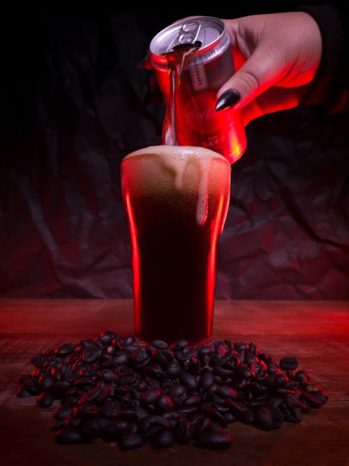 Woman Hand Holding Coca Cola Can over Glass near Coffee Beans