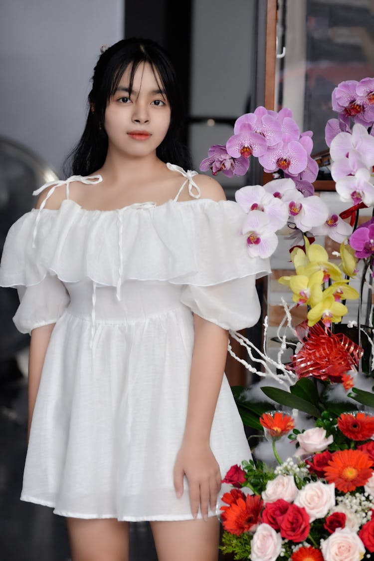 Woman In White Dress Standing Beside A Flower Bouquet