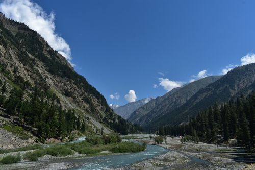 Free Majestic mountain valley with a flowing river and lush green forest under a clear blue sky. Stock Photo