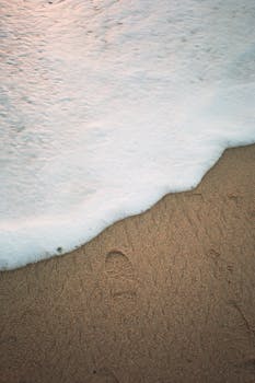 A tranquil beach scene with a footprint in the sand as ocean waves approach.