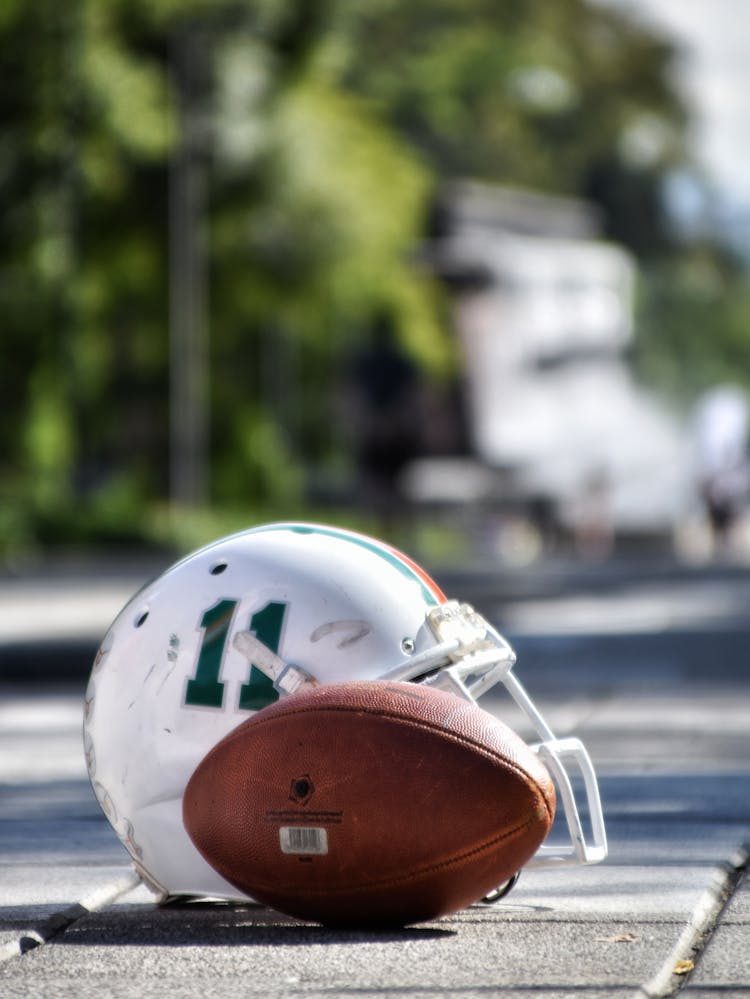 Football Helmet Beside Football On Gray Asphalt Road