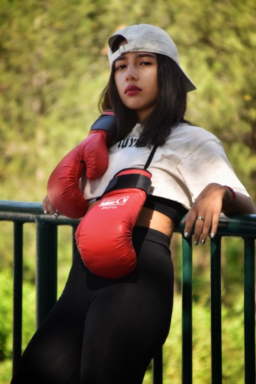 Free Confident young woman boxer posing with red gloves outdoors, leaning on railing. Stock Photo