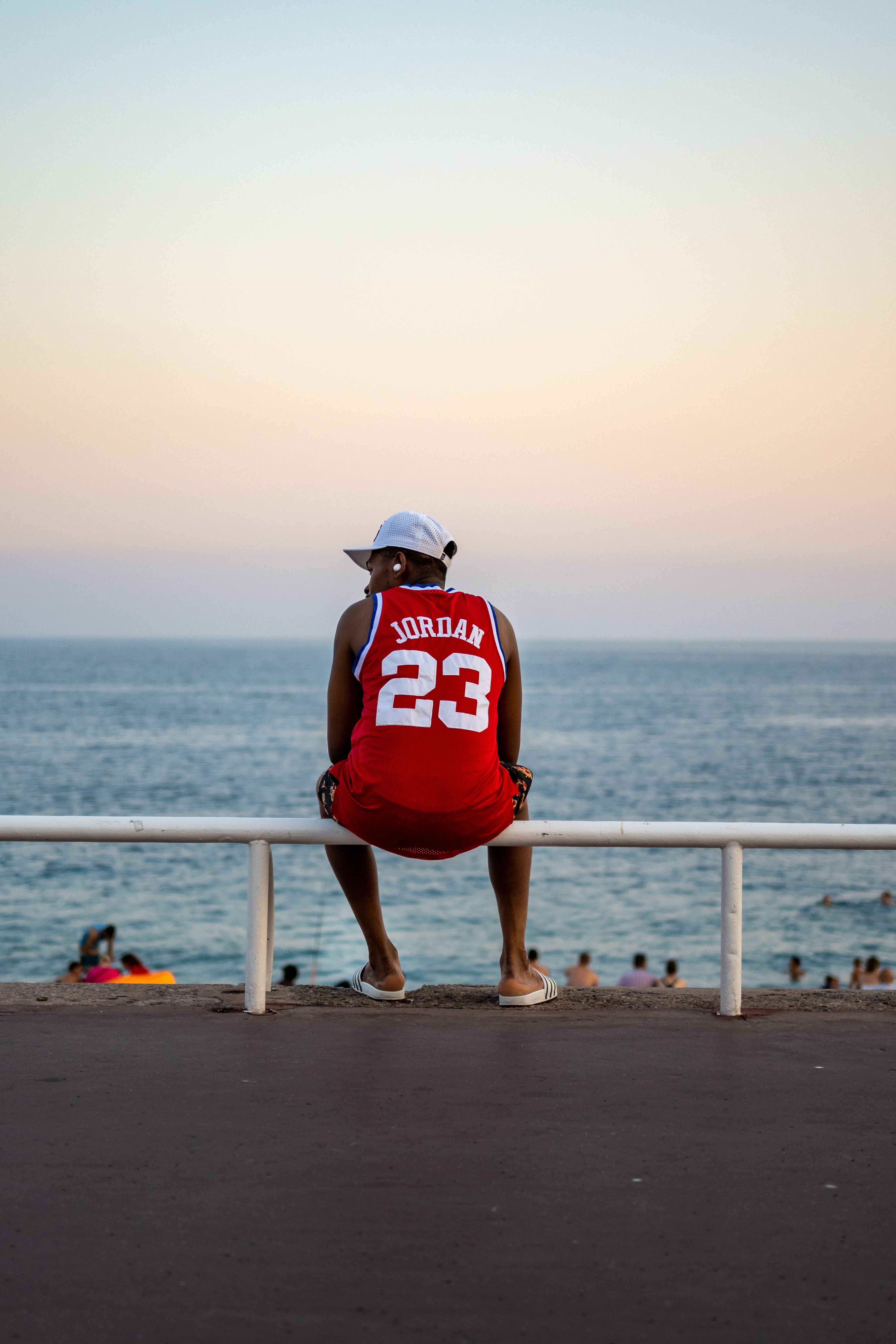 A man in a jersey relaxes by the sea in Nice at sunset, enjoying leisure time.