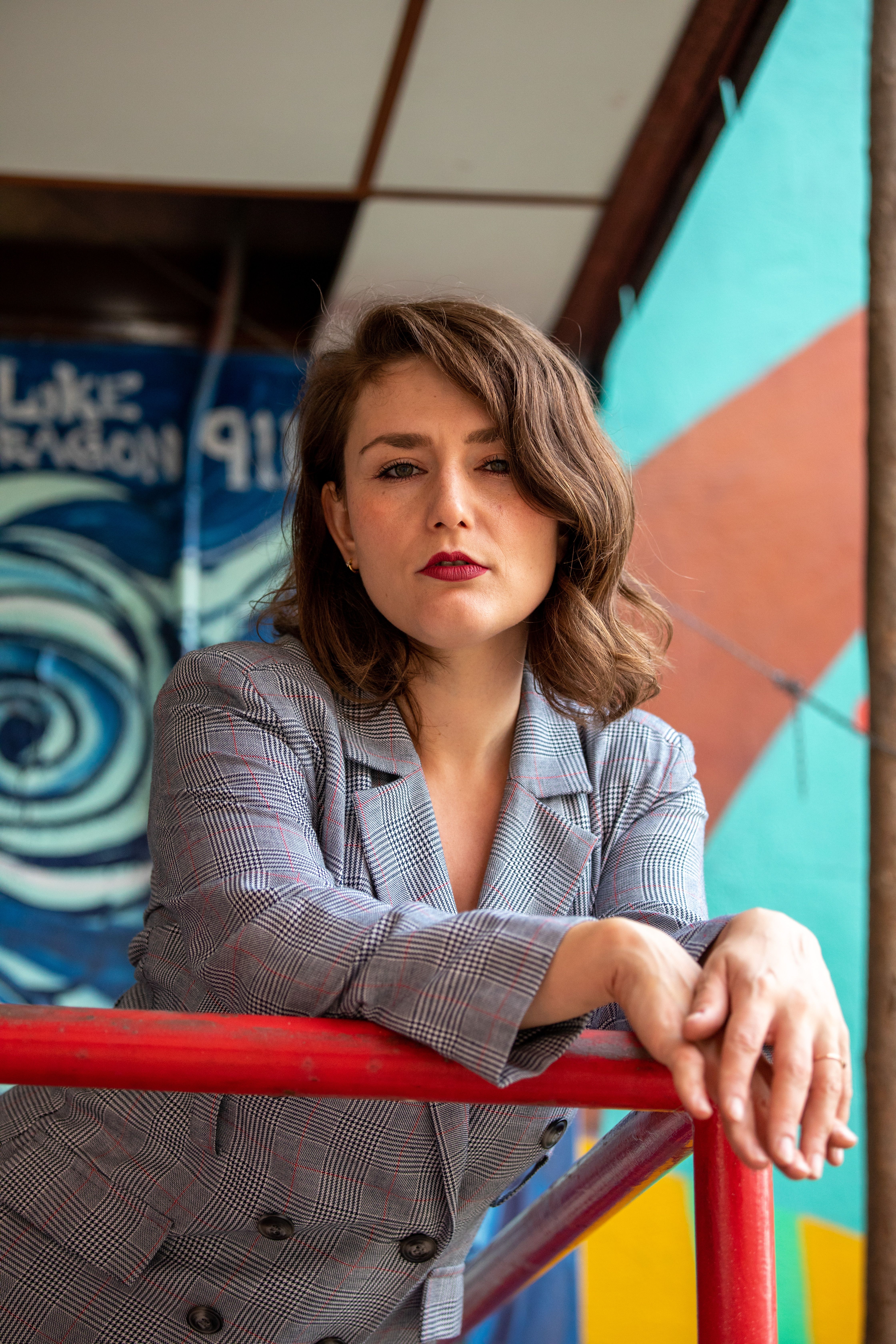 Confident woman in stylish blazer leaning on a red railing against an artistic background.