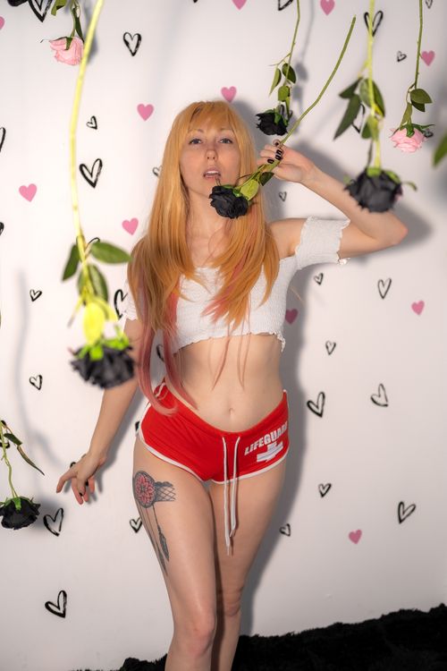 Free A fashionable model striking a pose amidst hanging flowers and a heart-patterned backdrop. Stock Photo