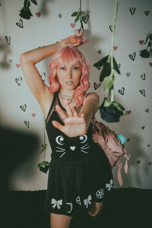 Free Creative portrait of a woman with pink hair amidst hanging flowers and heart decorations. Stock Photo