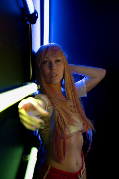 Free Portrait of a woman posing in vibrant neon lighting, creating a modern and stylish look. Stock Photo