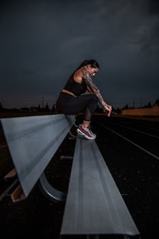 Woman in athletic wear sitting on a bench in a dark outdoor track setting.