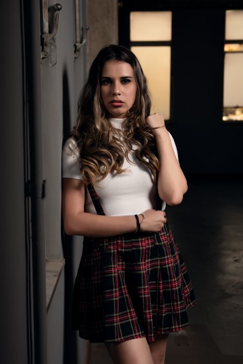 Free Fashionable woman posing in a plaid skirt and white top indoors, showcasing modern fashion. Stock Photo