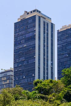 A modern high-rise building with sleek glass windows and lush greenery in the foreground.