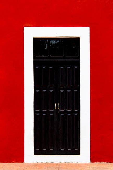 Elegant black wooden door set against a vibrant red wall with white trim. Urban minimalism at its best.