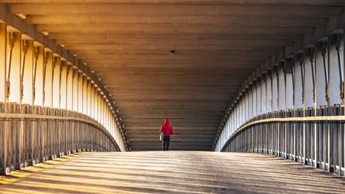 Free A lone figure in a red jacket walking under a bridge at sunset, casting long shadows. Stock Photo