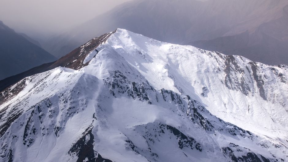 A breathtaking view of a snow-covered mountain peak amidst a cloudy sky, showcasing nature's beauty.