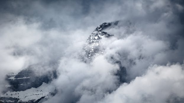 A stunning view of a snow-covered mountain peak shrouded in dramatic clouds, creating a mysterious atmosphere.