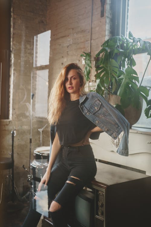 Woman in Black Tank Top and Blue Denim Jeans Sitting on Black Chair