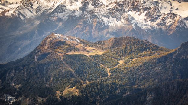 Stunning aerial view of lush green valleys and snow-capped peaks in the Alps during winter.