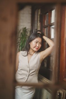 Elegant portrait of a woman leaning against a window with natural light and pensive expression.