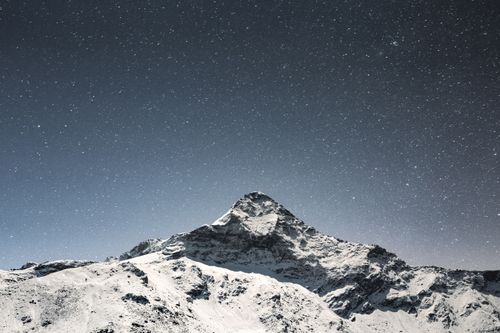 Free A mesmerizing view of a snow-covered mountain with a star-filled night sky. Stock Photo