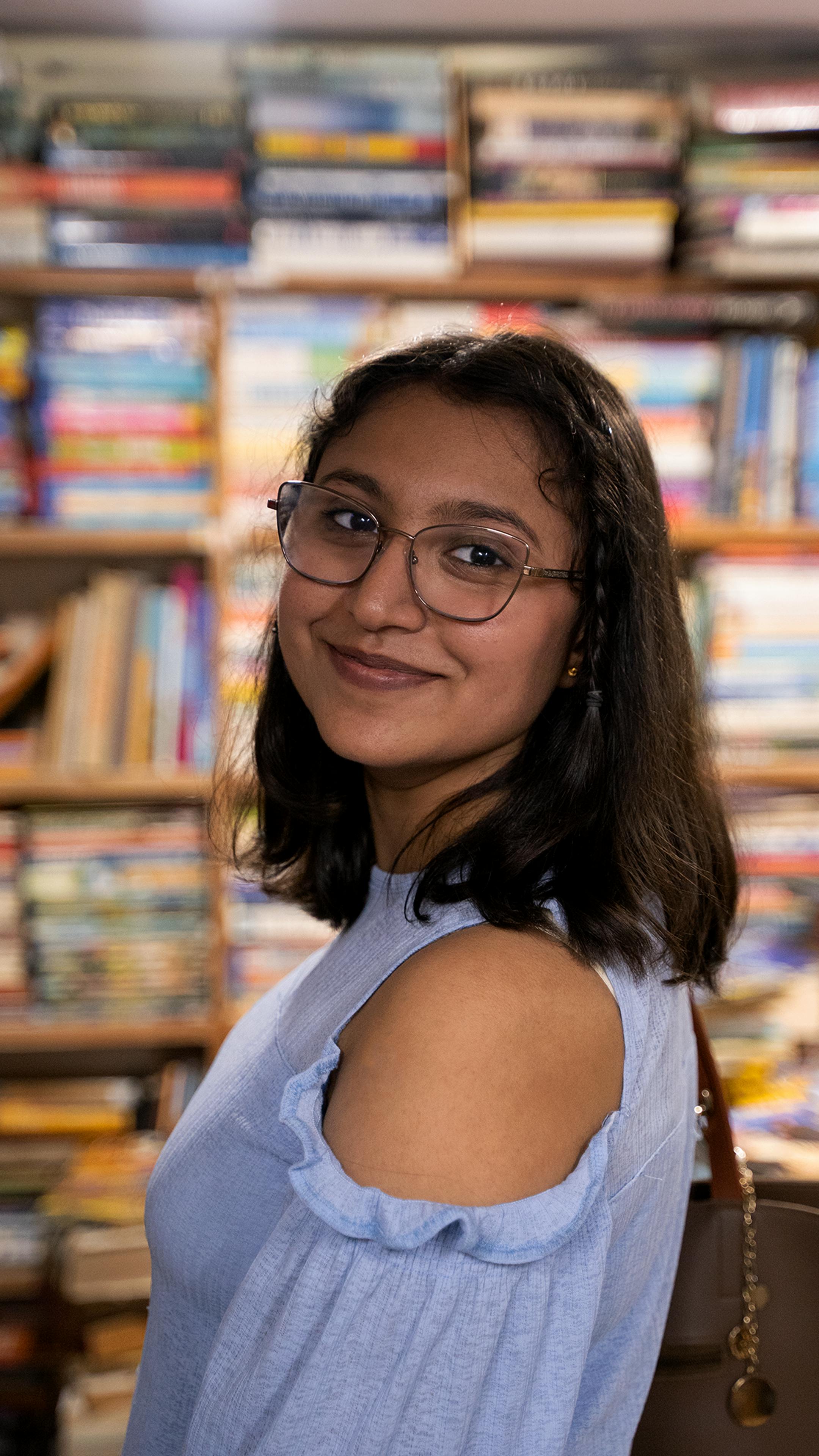 Portrait of a smiling young woman with glasses in a colorful bookstore, offering a warm and inviting atmosphere.