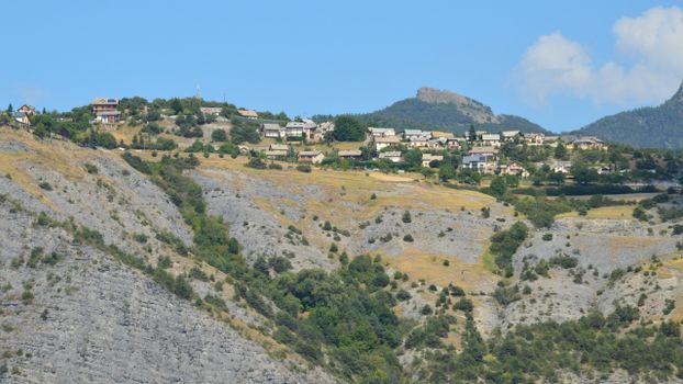 Picturesque rural village nestled on a hillside with eroded terrain under a bright blue sky.