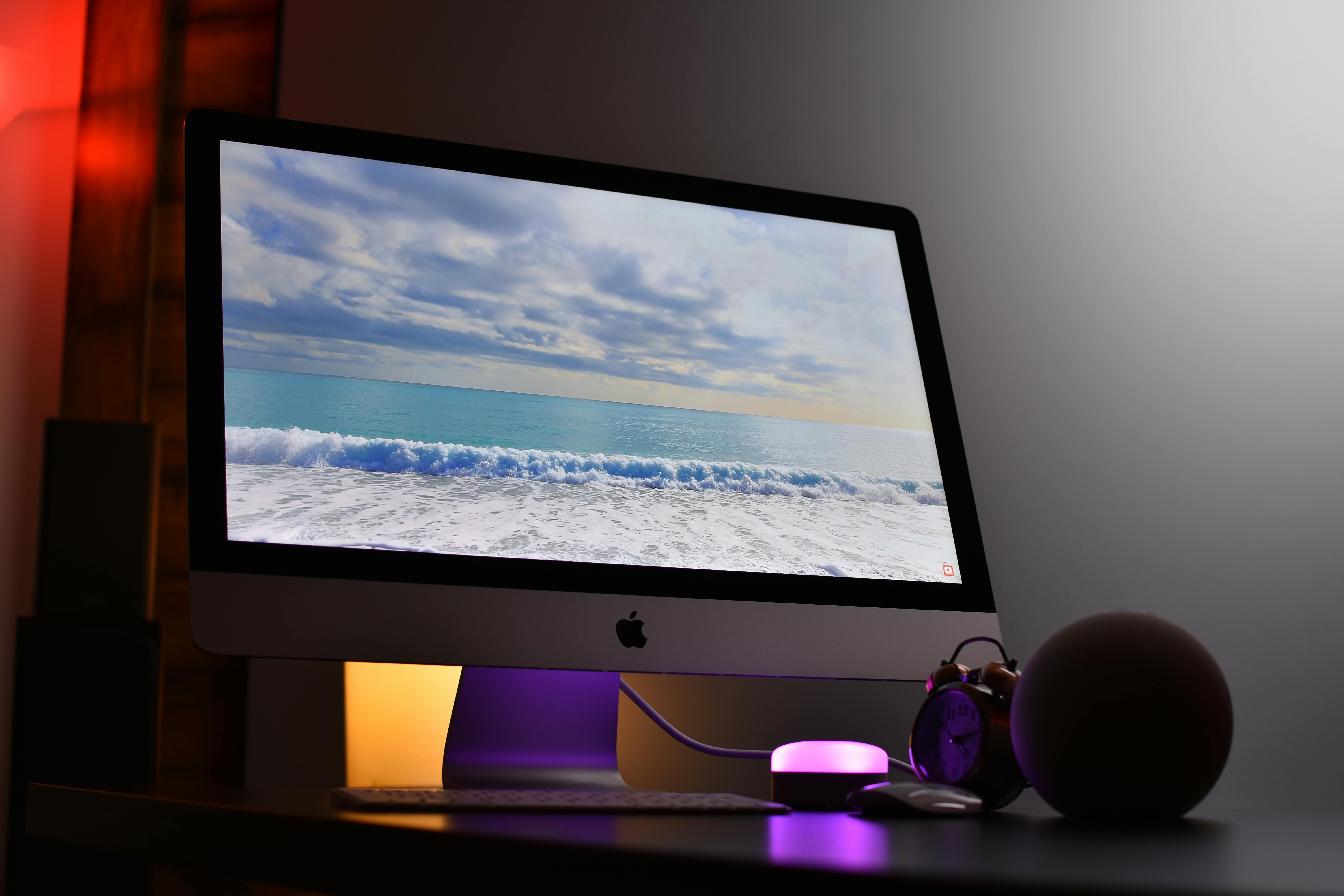 Apple iMac displaying ocean view. Elegant workspace with ambient lighting.