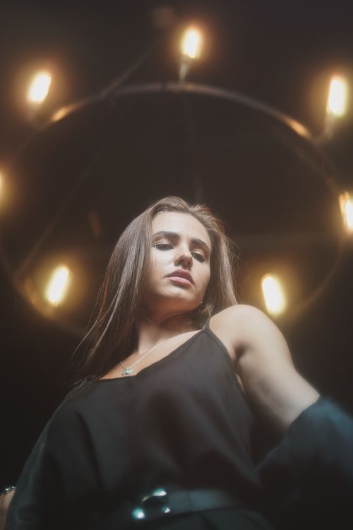 Free Low-angle portrait of a woman in a black sleeveless top under chandelier lights. Stock Photo