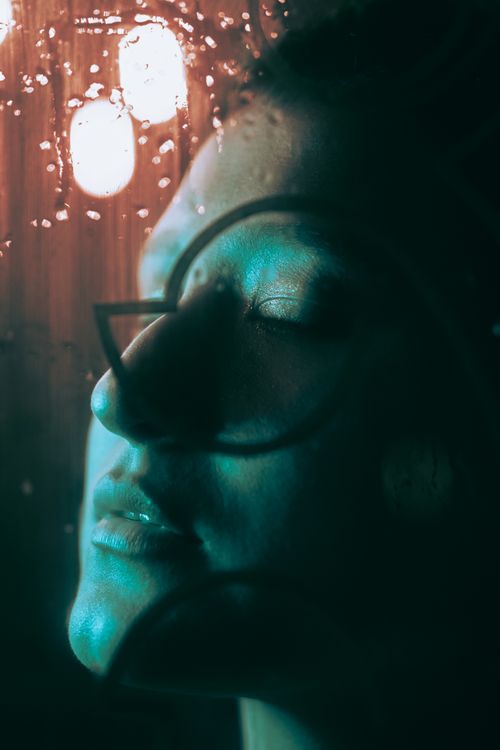 Free Artistic portrait of a woman with closed eyes, behind a rainy glass window, evoking peace and tranquility. Stock Photo