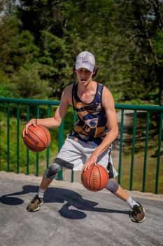 A sporty young man dribbles two basketballs during outdoor practice on a sunny day.