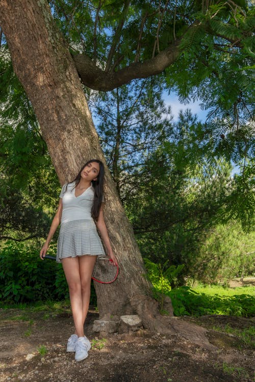 Young Beautiful Woman Wearing Tennis Suit and Leaning on a Tree