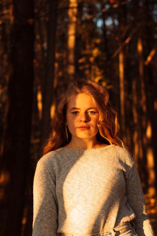 Free A woman with ginger hair standing in a sunlit forest during autumn. Stock Photo
