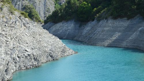 Free A vibrant turquoise river flows between rocky cliffs in a serene mountainside landscape. Stock Photo