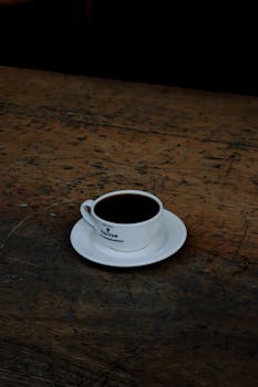 A ceramic cup of coffee rests on a rustic wooden table, offering a cozy and inviting scene.