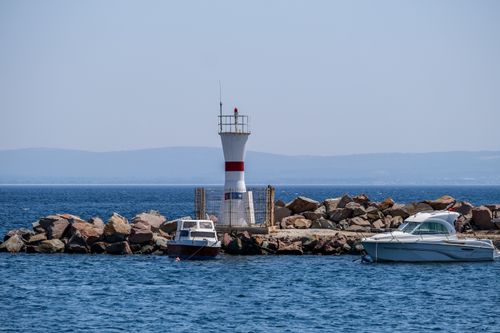 Free View of boats moored near Bozcaada lighthouse in Turkey, under a clear blue sky. Stock Photo