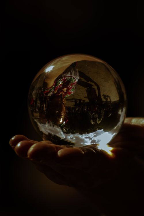 Free A mystical reflection captured inside a glass sphere held by a hand, creating an artistic play of light and shadow. Stock Photo