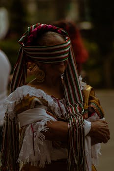 Elderly woman in traditional Mexican clothing with a vibrant blindfold and crossed arms.