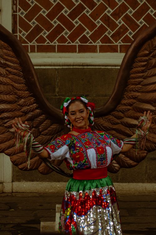 Free Woman in traditional Mexican attire smiling in front of ornate wings in Puebla. Stock Photo