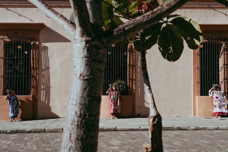 Femmes en tenue traditionnelle sur un trottoir à Oaxaca, projetant des ombres au soleil.