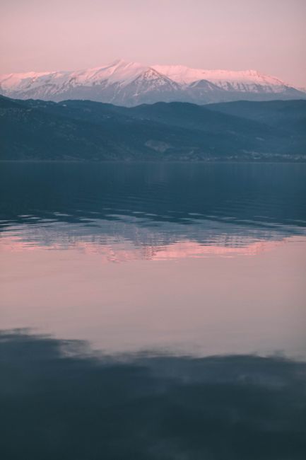 Beautiful sunset view of snowy mountains reflecting in Ioannina's tranquil waters.