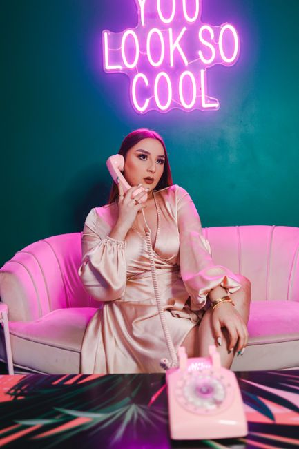 Stylish woman in satin dress posing by neon sign indoors. Fashionable and glamorous decor.