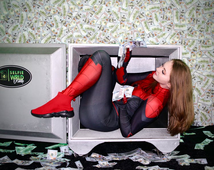 Woman In Spiderman Costume Inside A Box Holding Paper Money