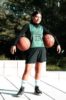 Teen player in sports gear holding two basketballs outdoors, Mexico City