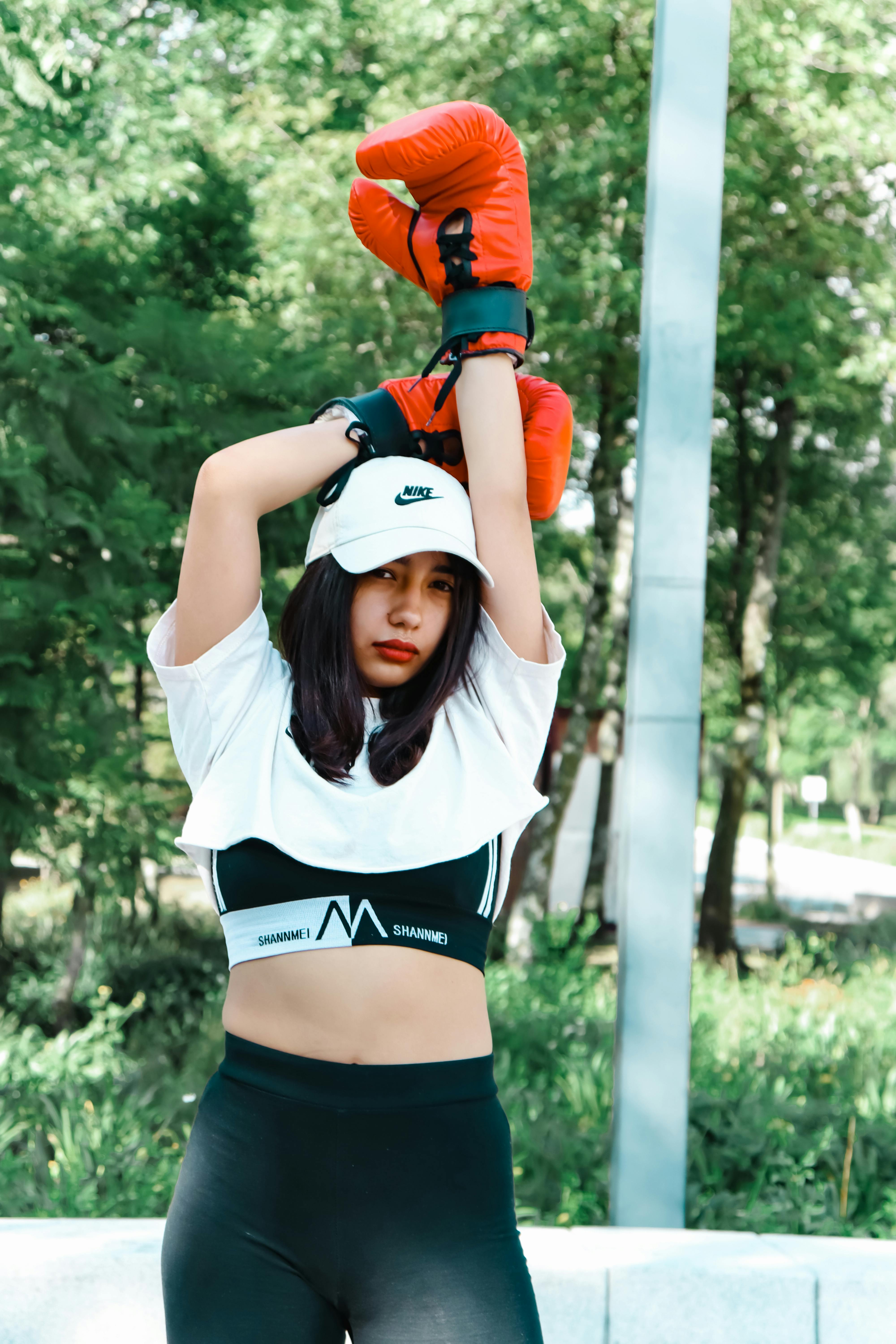 Young woman in sportswear with boxing gloves, exercising outdoors in a park setting.